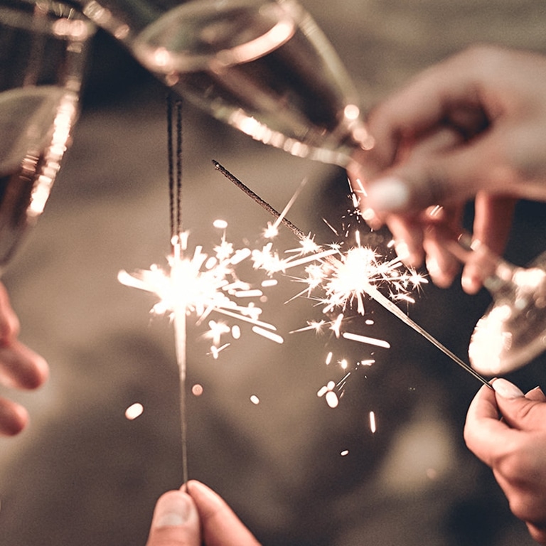 Feiern mit einem prickelnden Toast: Hände, die Gläser mit Champagner und Wunderkerzen halten und die Wärme und Freude eines besonderen Moments einfangen.