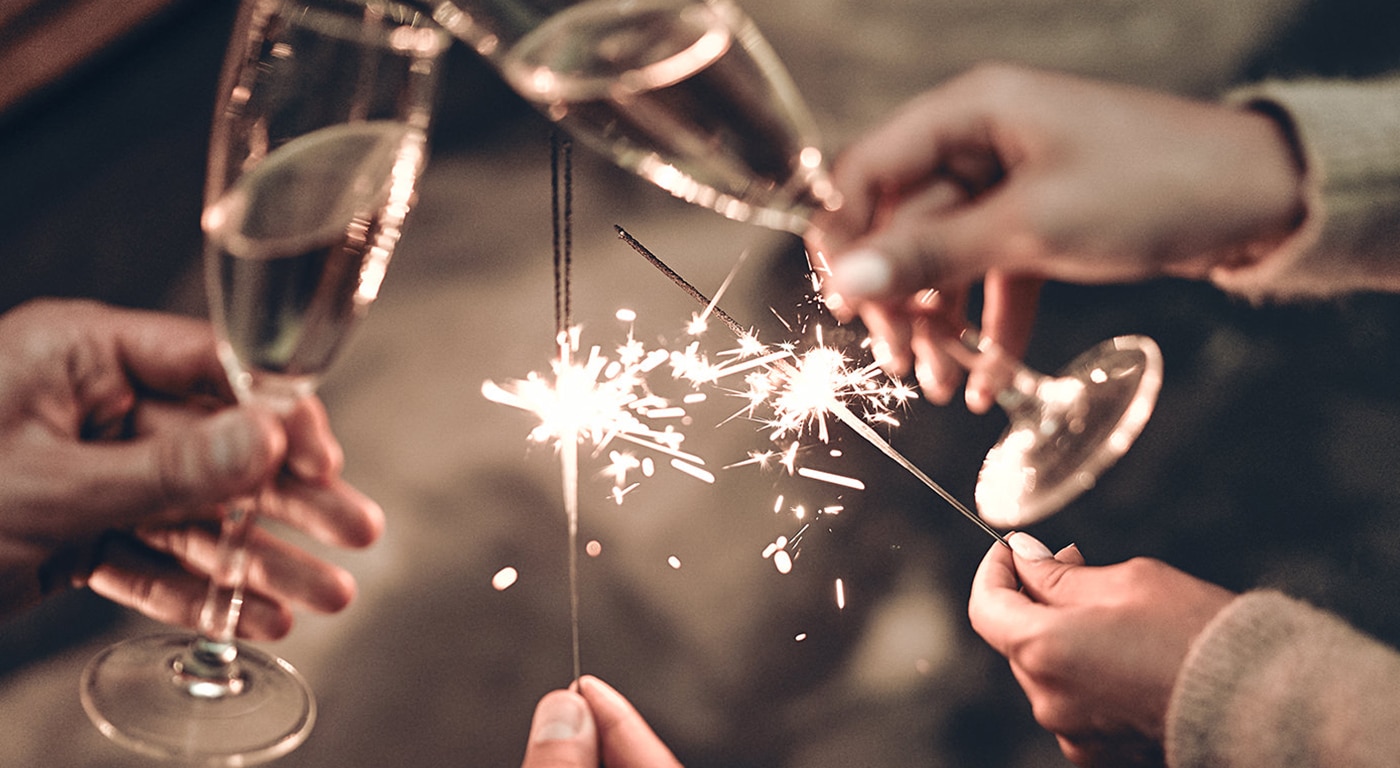 Feiern mit einem prickelnden Toast: Hände, die Gläser mit Champagner und Wunderkerzen halten und die Wärme und Freude eines besonderen Moments einfangen.
